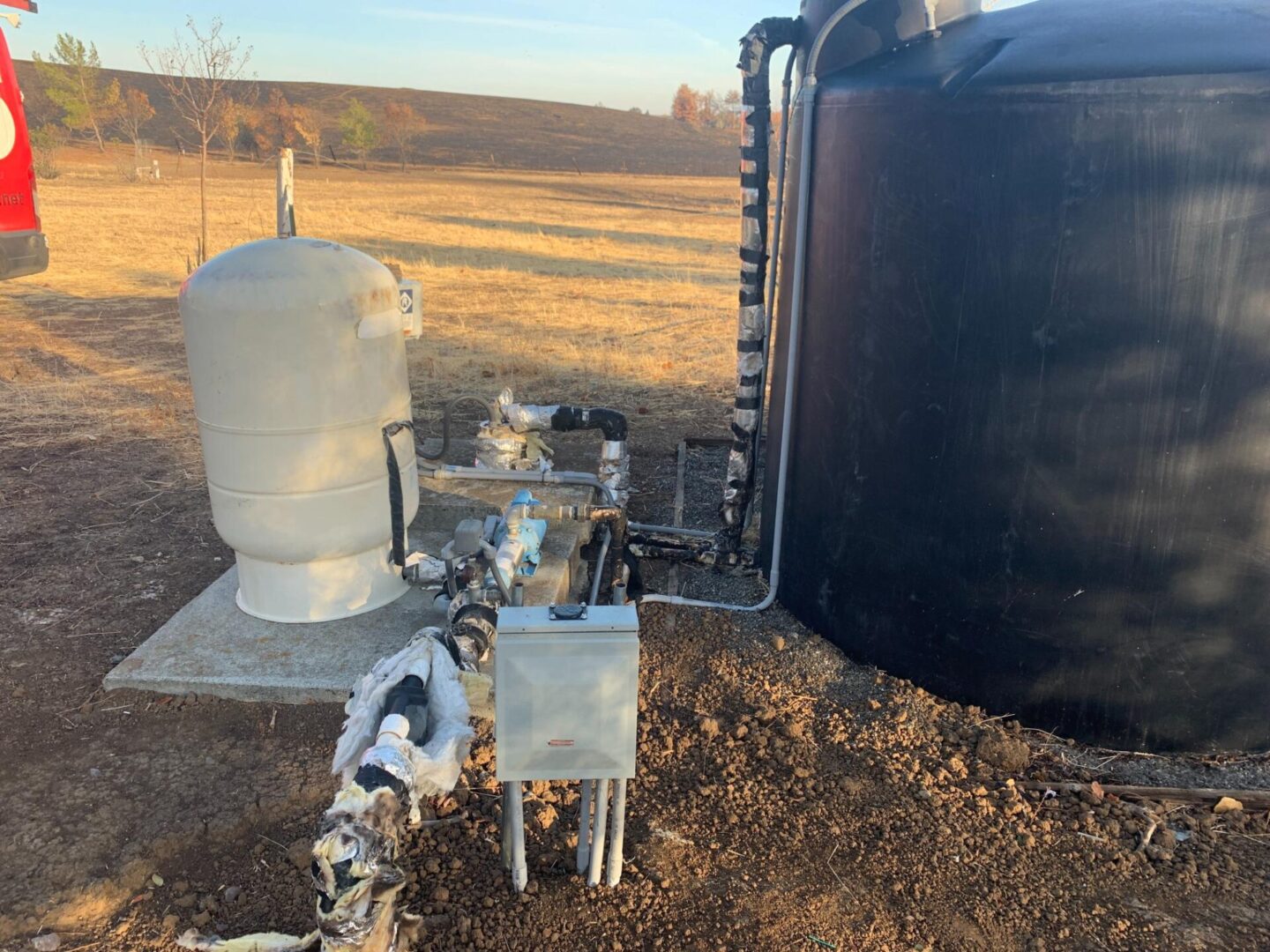 A black tank sitting next to a metal pipe.