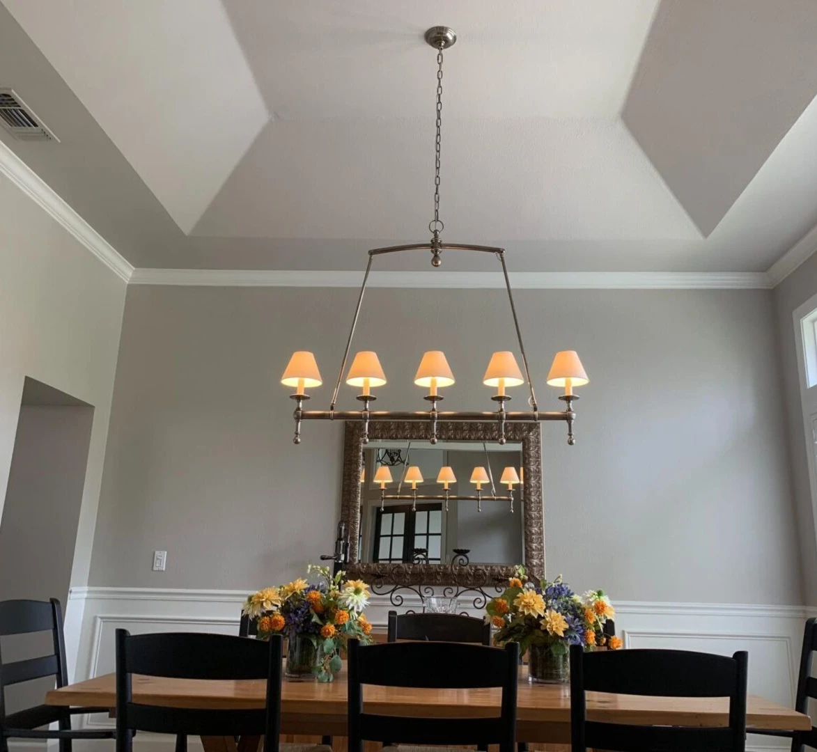 A dining room with a table and chairs, a mirror and a chandelier.